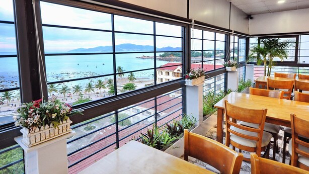 A restaurant with large windows offering a view of the beach and ocean. - Arise Hotel (Nha Trang)