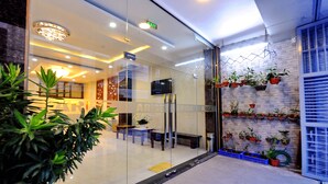 A modern hotel lobby with a glass entrance, a reception desk, and a wall decorated with potted plants. - Arise Hotel (Nha Trang)