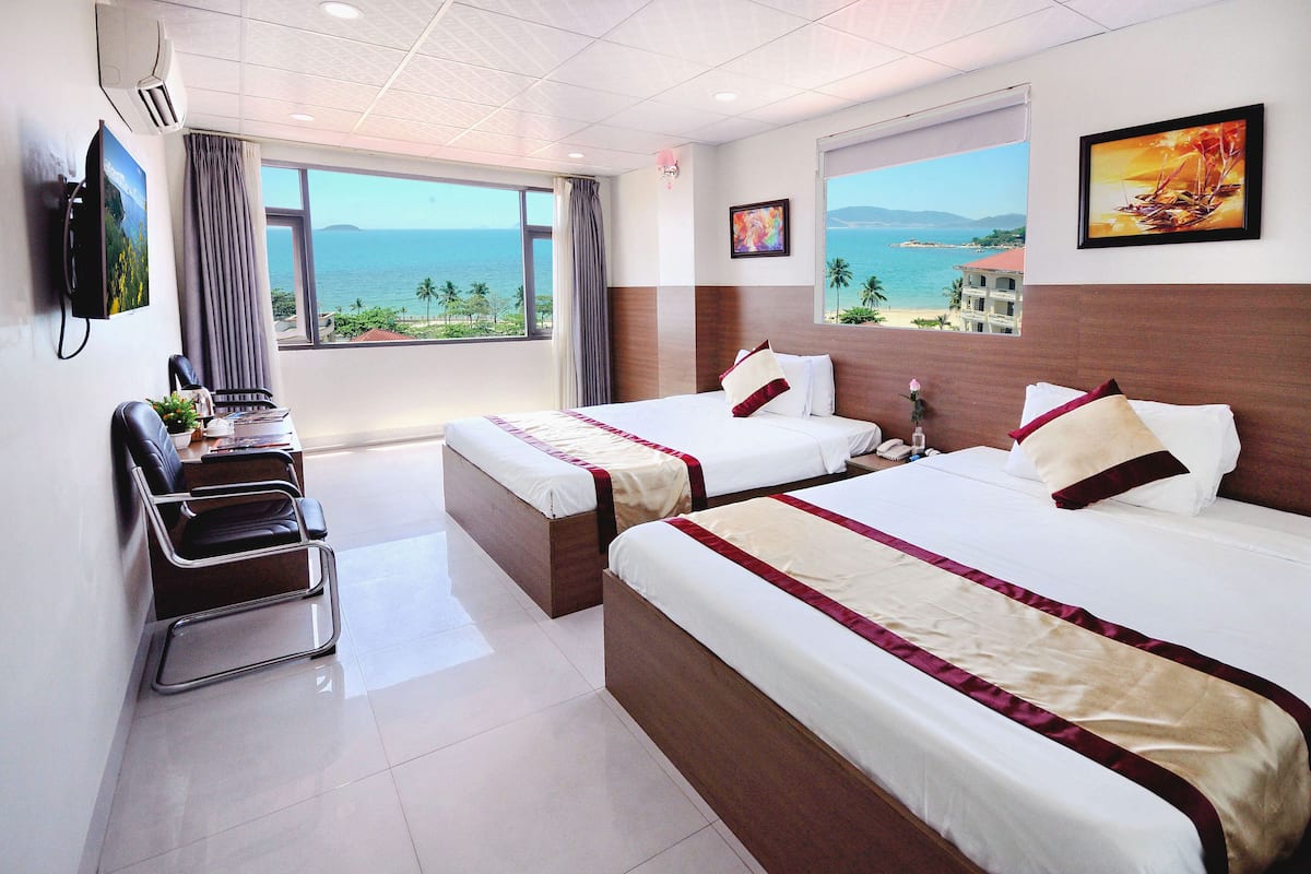 Une chambre d’hôtel avec deux lits, un bureau et vue sur la mer.