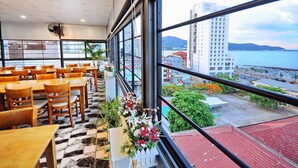 A restaurant with wooden tables and chairs, large windows with a view of a city and water body. - Arise Hotel (Nha Trang)