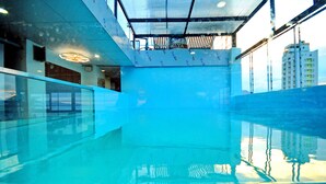 An indoor swimming pool with clear water, a glass barrier, and a ceiling with visible structural elements. - Arise Hotel (Nha Trang)