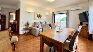 Una sala de estar con sofá, una mesa de comedor con sillas, televisor y un ventanal grande.