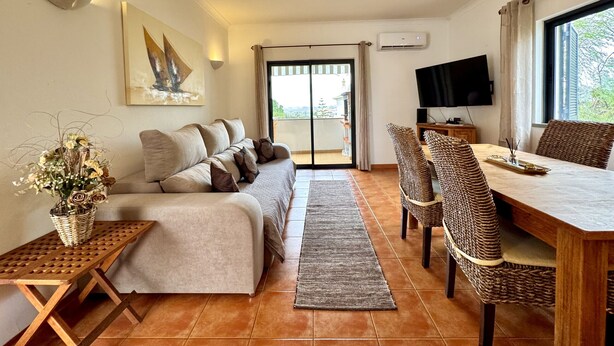 Una sala de estar con sofá, una mesa de comedor con sillas, televisor y puerta al balcón.