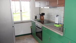 Una cocina compacta con gabinetes verdes, horno empotrado y ventana que proporciona luz natural.