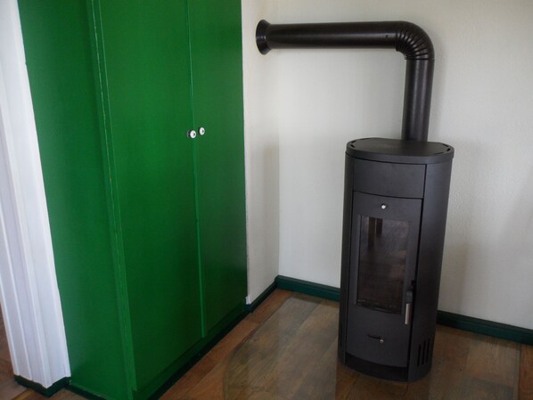 A black wood-burning stove with a chimney, positioned next to a green door and a white wall. - Vacation homes in the hamlet of Krüger with private lake access (Wuthenow)