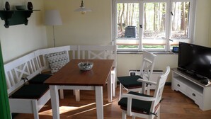 Un comedor con una mesa de madera, sillas blancas, un cuenco sobre la mesa y un televisor en un mueble.