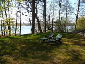 A grassy area with two green striped chairs facing a body of water, surrounded by trees. - Vacation homes in the hamlet of Krüger with private lake access (Wuthenow)