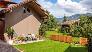 Une maison en bois avec un toit en pente et une petite terrasse agrémentée de chaises et de plantes en pot.