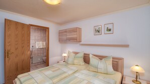 Una camera da letto con un letto, comodini, un armadio in legno, un termosifone e due quadri appesi al muro.