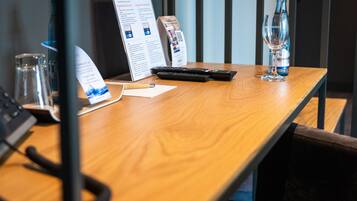 A wooden table with a menu, a glass, a bottle, and a remote control.