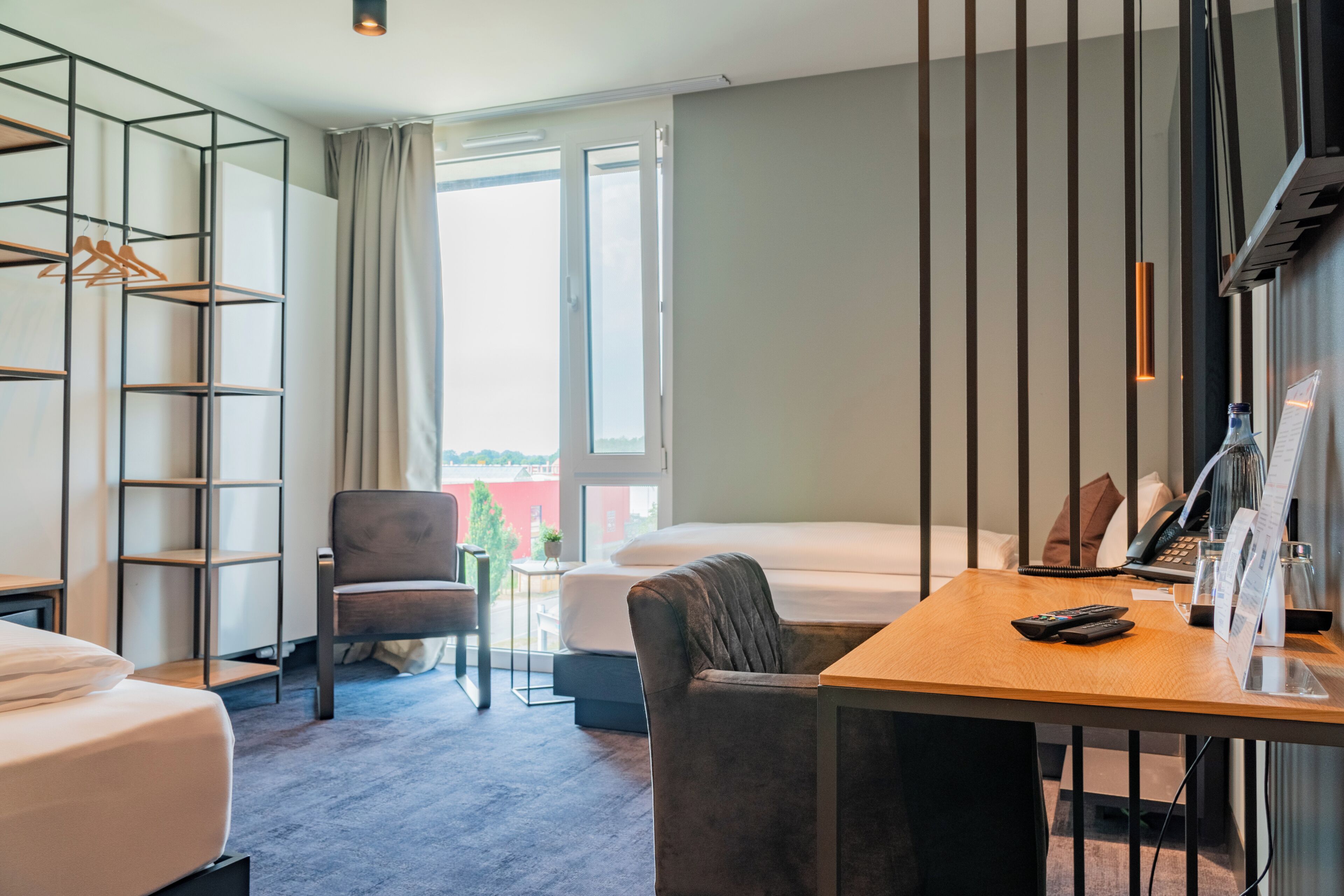 Habitación de hotel con cama, escritorio, silla, armario y ventana con cortinas.