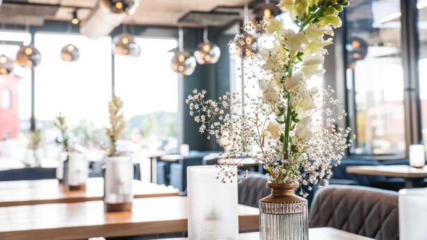 Interior de un restaurante con mesas, sillas y jarrones decorativos con flores.