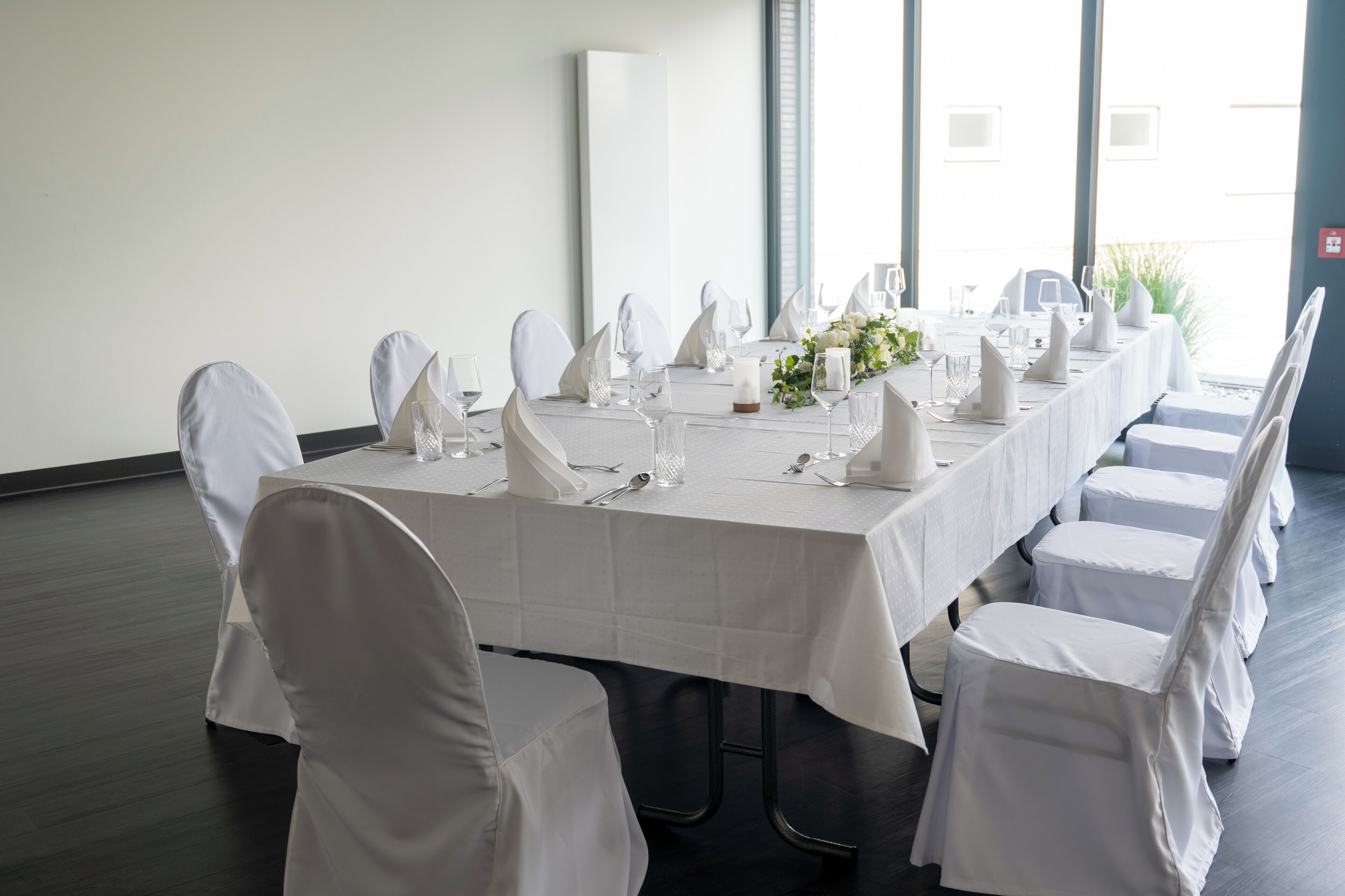A long dining table with white tablecloth and chairs, set for a formal meal.