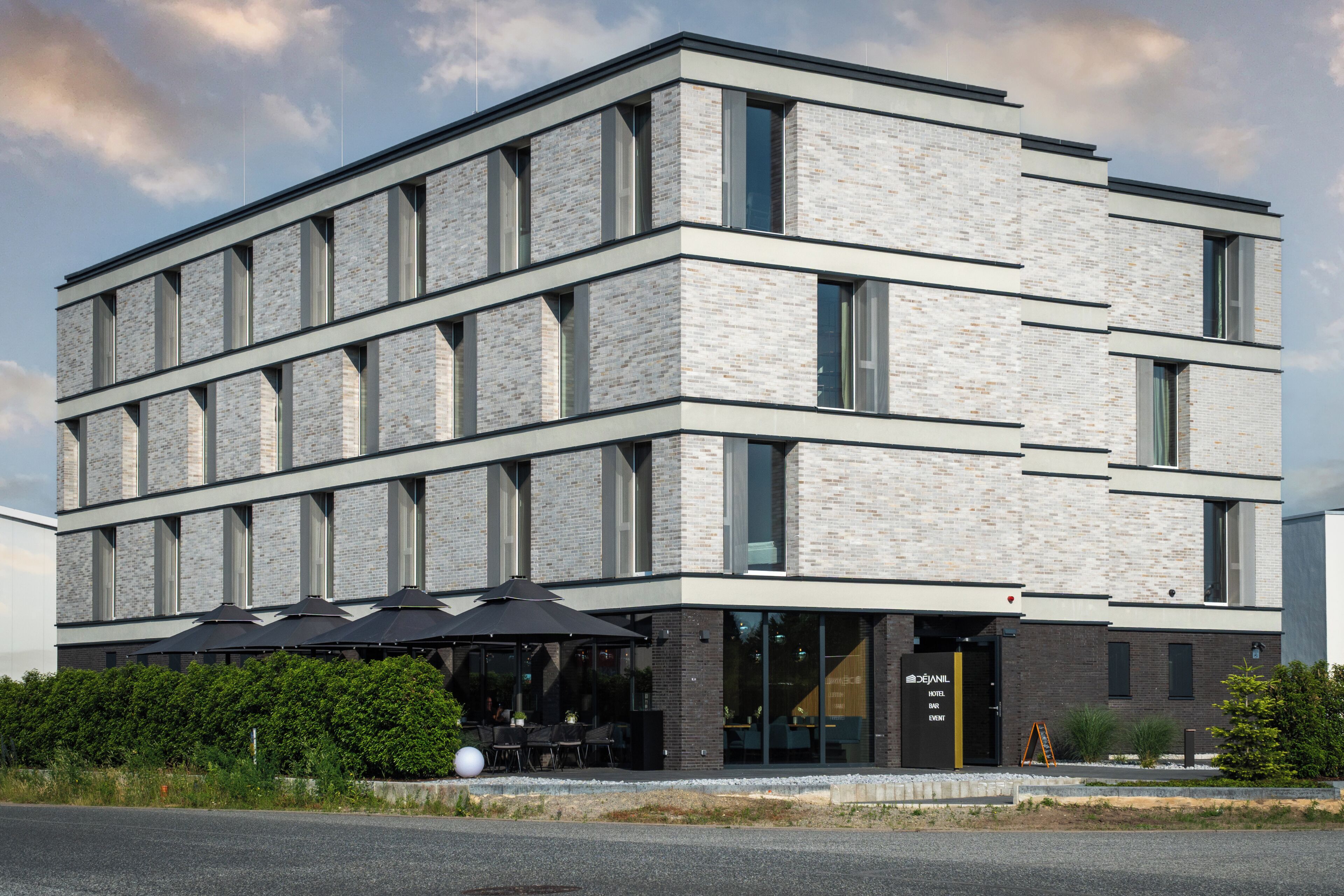 A modern hotel with a brick facade, large windows, and outdoor seating.