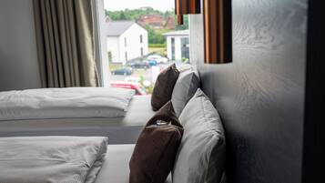 Een hotelkamer met twee bedden, een raam met gordijnen en uitzicht op een straat met geparkeerde auto's en een gebouw.