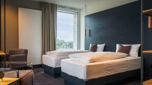 Una habitación de hotel moderna con dos camas, un espacio de descanso y un ventanal con vistas al exterior.