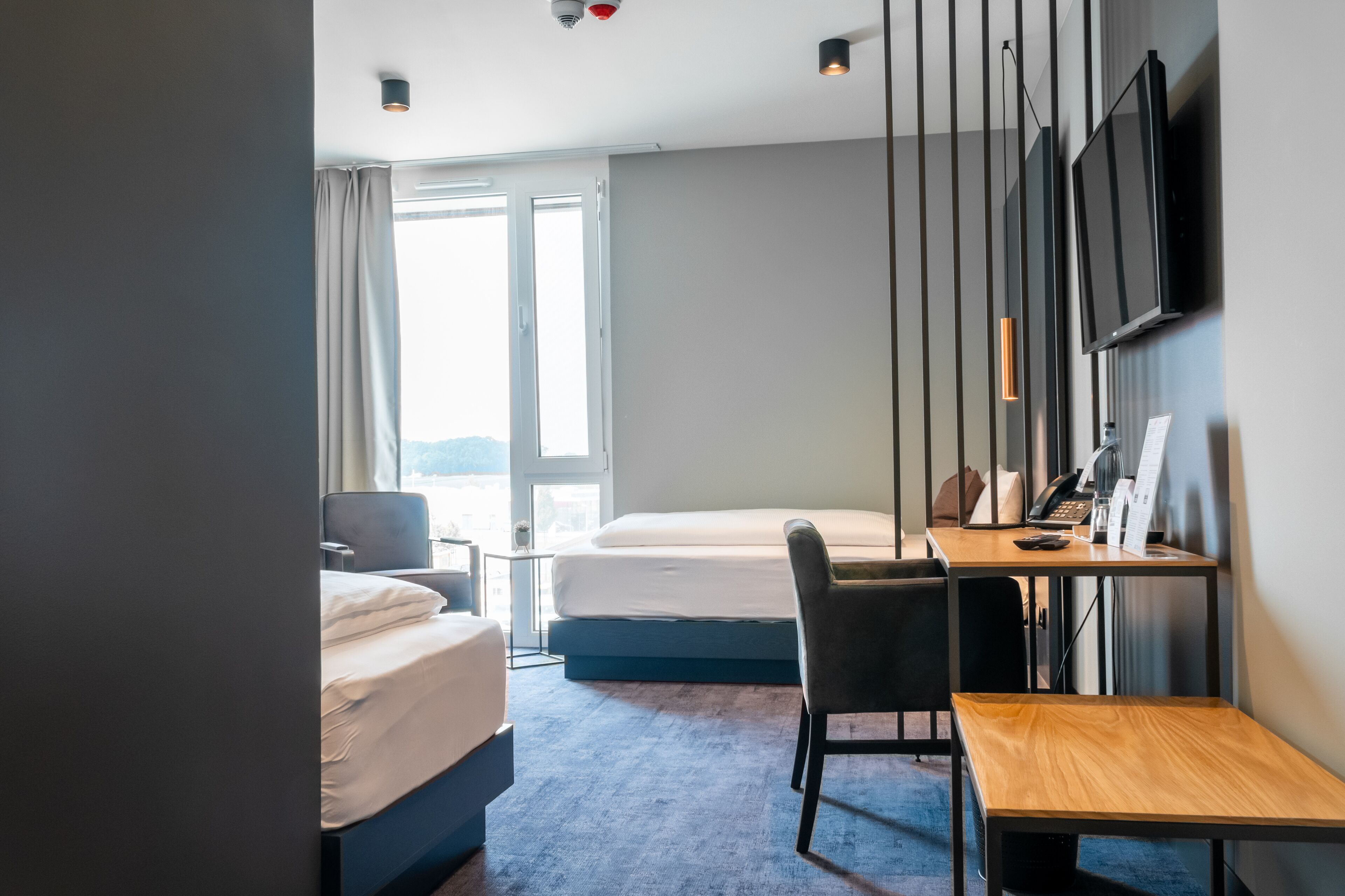 A hotel room with two beds, a desk, a chair, a TV, and a window with curtains.