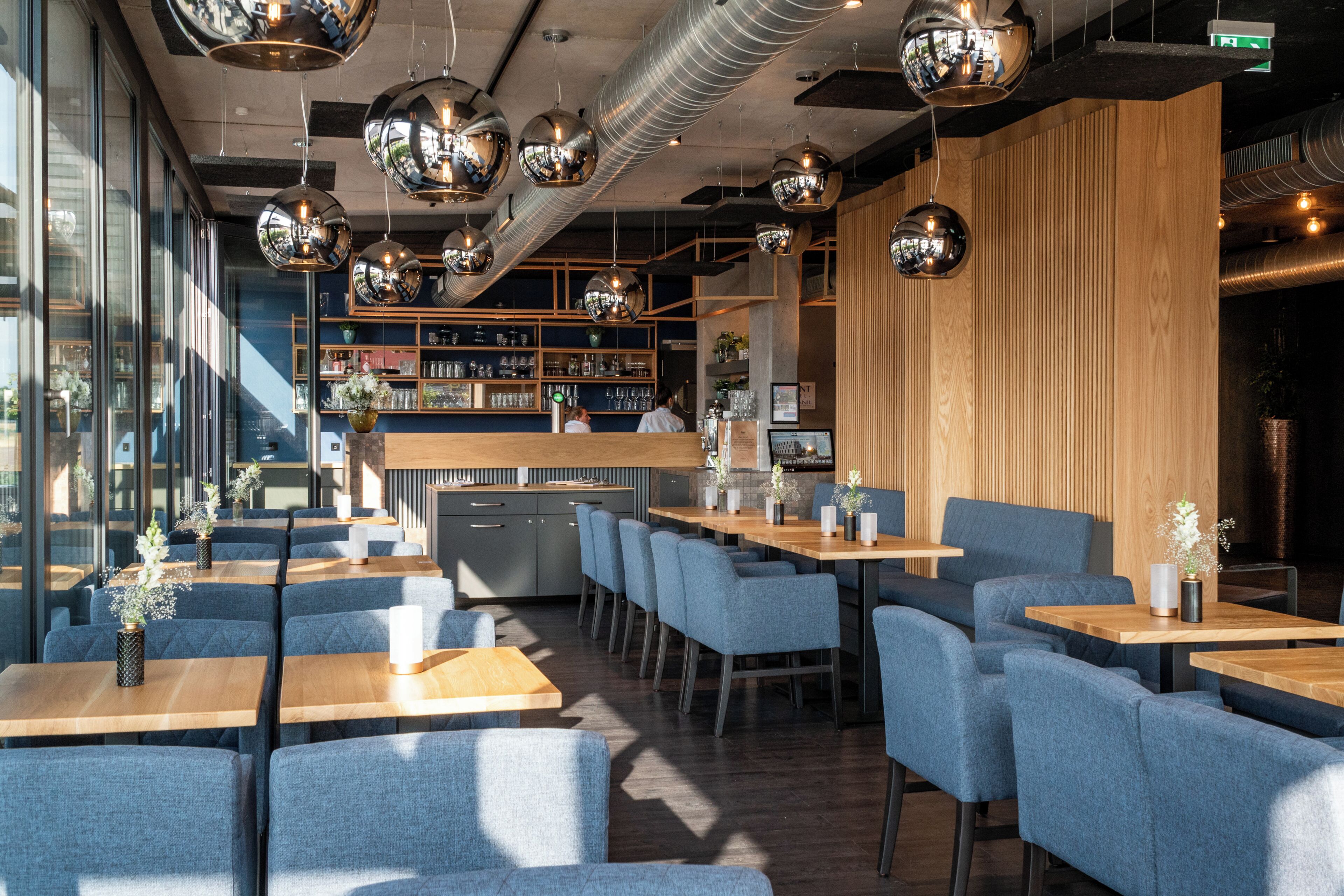 Un interior de restaurante moderno con mesas de madera, sillas tapizadas en azul y elegantes lámparas colgantes esféricas.