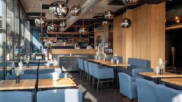 A modern restaurant interior with wooden tables, blue upholstered chairs, and reflective spherical pendant lights.