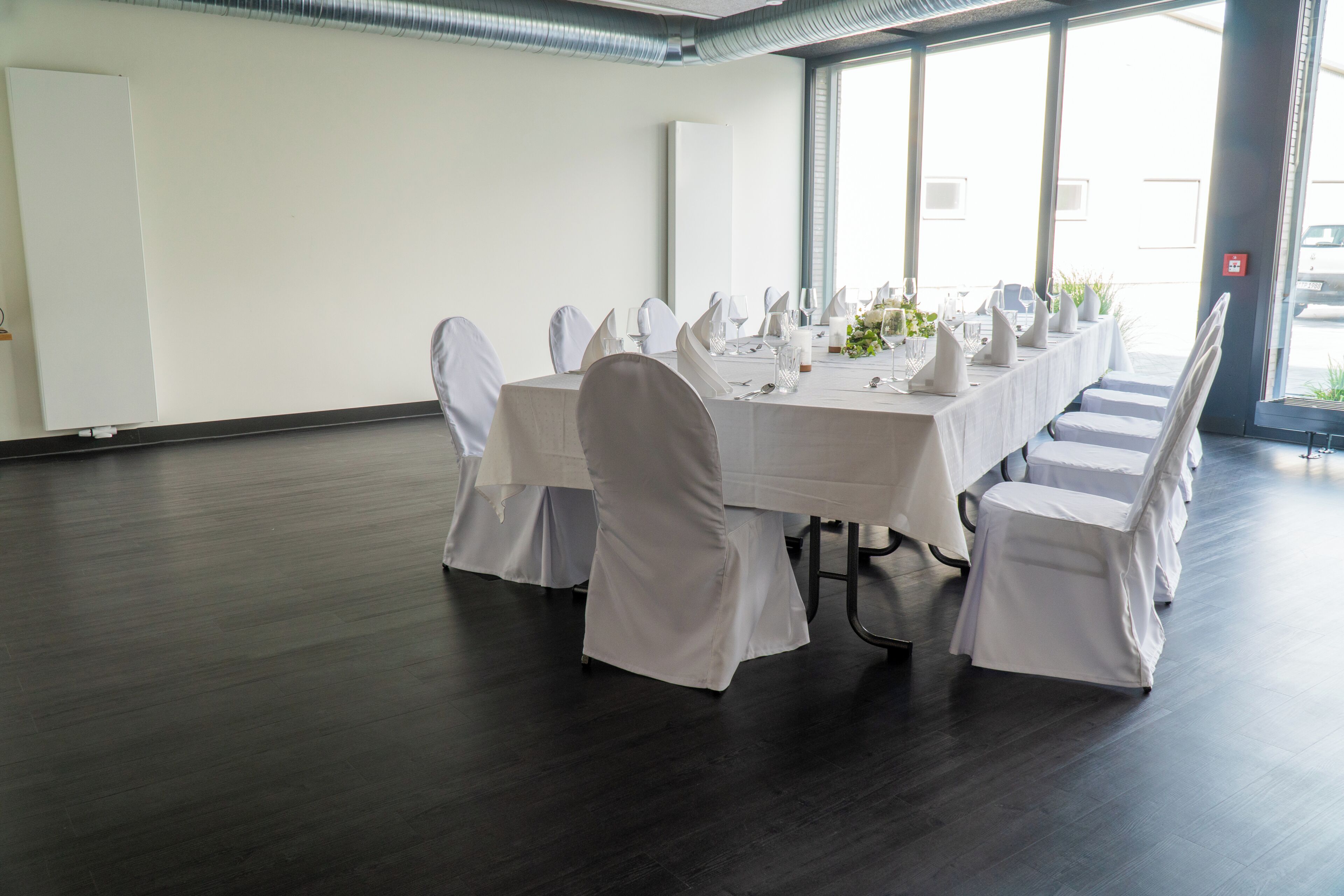Un salón de conferencias con una larga mesa dispuesta para una reunión, sillas blancas y vistas al exterior a través de amplias ventanas.