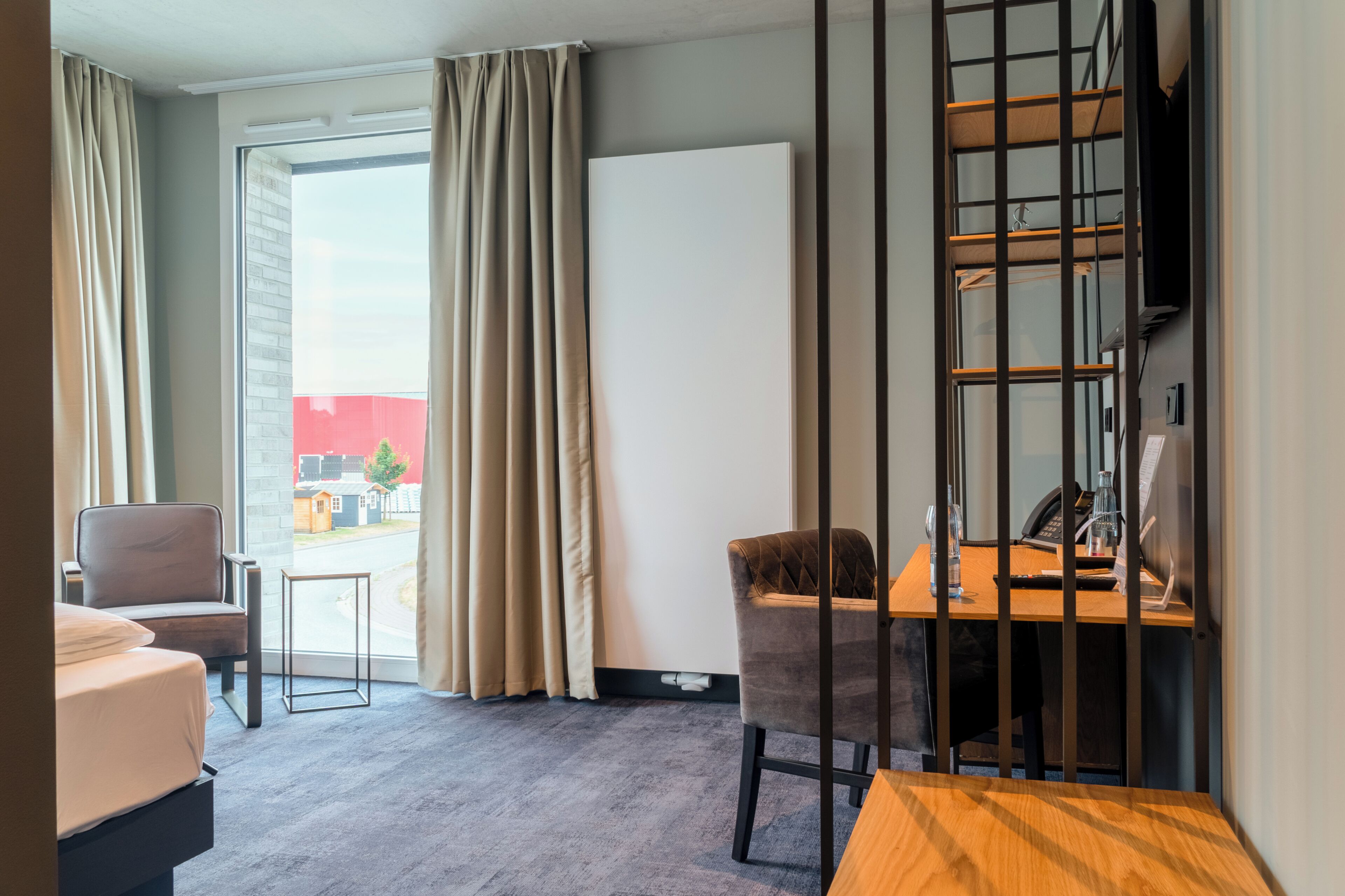 Habitación de hotel con cama, escritorio, una silla y vistas al exterior.