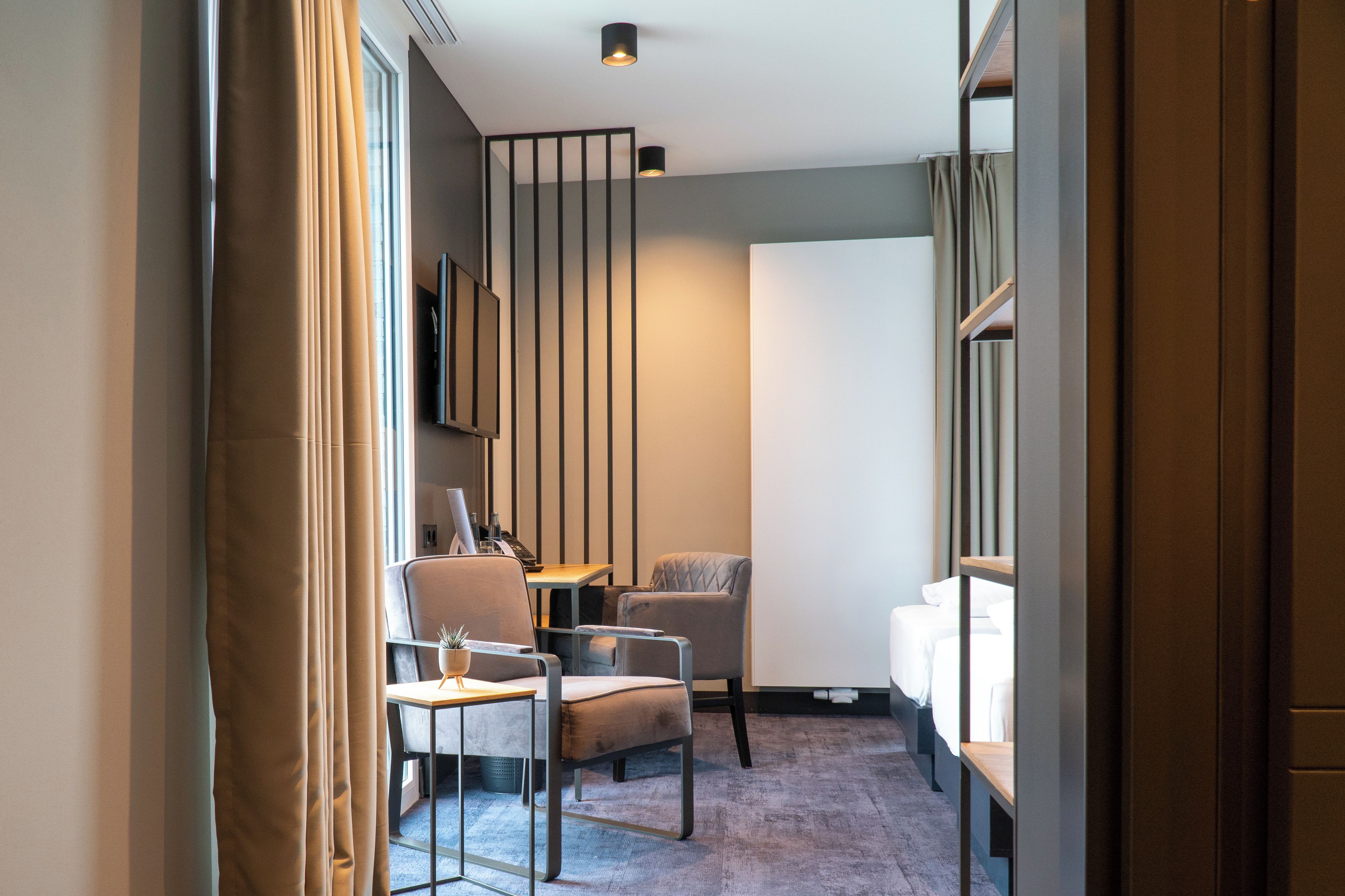 Una habitación de hotel moderna con una zona de estar, un escritorio y un ventanal grande.
