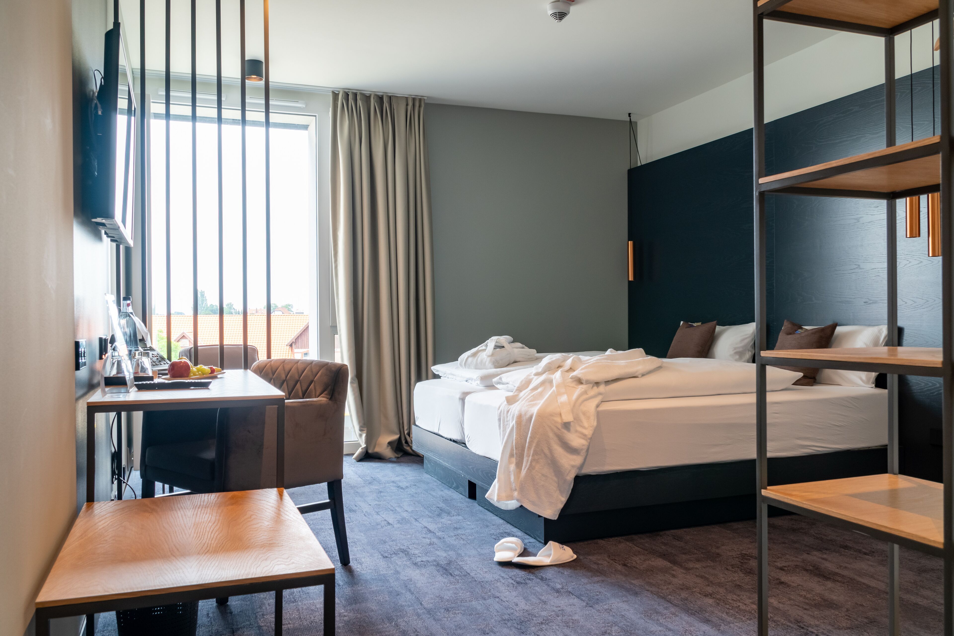 A hotel room with a bed, a desk, a chair, and a window with curtains.