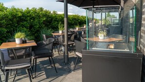 Un patio al aire libre con mesas y sillas, plantas en macetas y un cerramiento de vidrio.