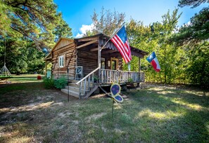 Eine rustikale Holzhütte mit Veranda, einer amerikanischen Flagge und einer französischen Flagge.