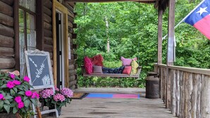 A wooden porch with a signboard, potted flowers, and a hammock. - Log Cabin - TINY HOUSE on acreage (Montgomery)
