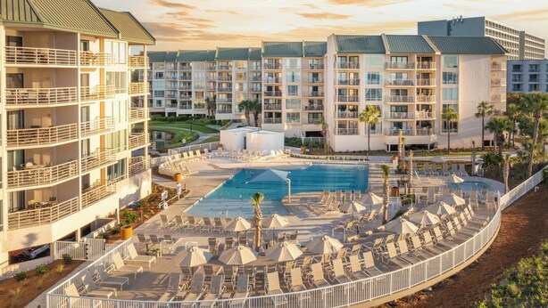 A hotel with multiple floors, a central pool area with sun loungers and umbrellas, and a surrounding landscaped area with palm trees. - 3326 Villamare -Ocean Front Villa Complex  - Fully Renovated and New Pools! (Hilton Head Island)