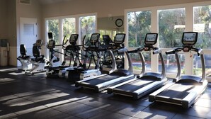 A gym with multiple treadmills and elliptical machines, large windows, and a clock on the wall. - 3326 Villamare -Ocean Front Villa Complex  - Fully Renovated and New Pools! (Hilton Head Island)