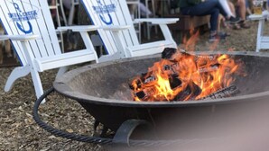 A fire pit with burning logs surrounded by white Adirondack chairs with blue logos. - 3326 Villamare -Ocean Front Villa Complex  - Fully Renovated and New Pools! (Hilton Head Island)