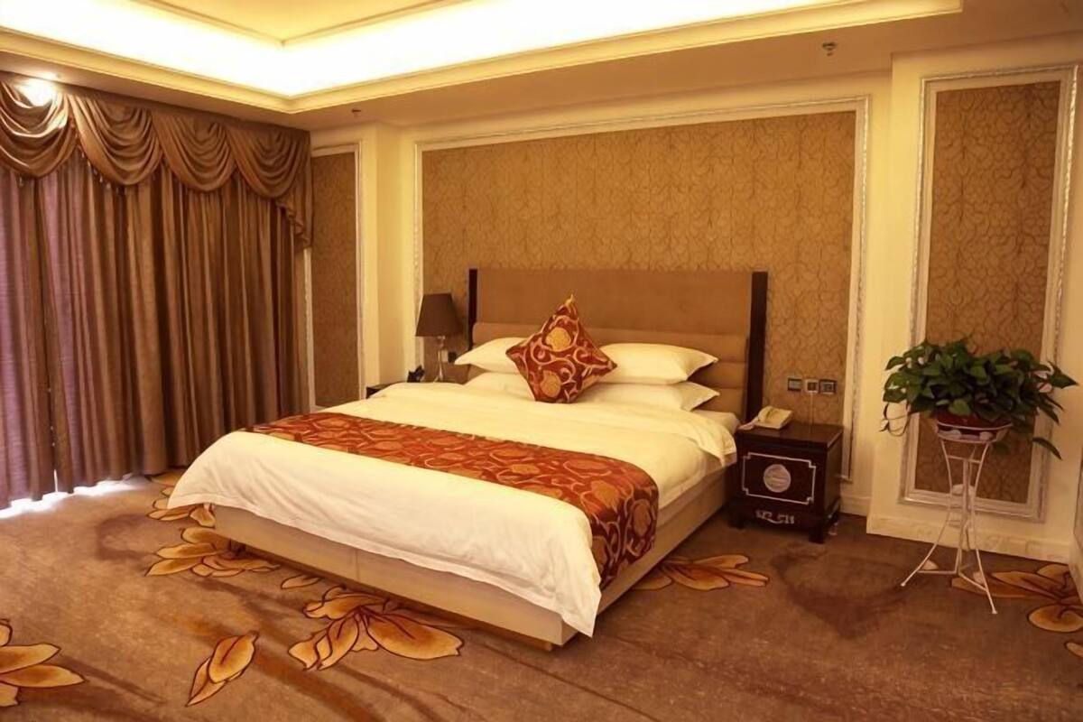 Habitación de hotel con una cama grande, una mesita de noche con lámpara, teléfono y una planta en maceta.