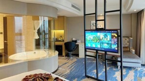 Una camera d'albergo moderna con una vasca da bagno a semicircolo, una scrivania con un computer, una televisione e un'area salotto.