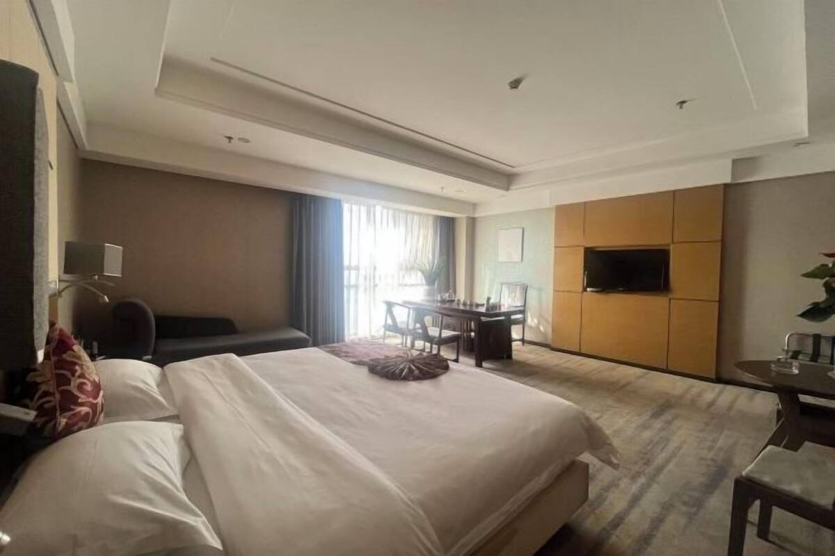 Habitación de hotel con cama, escritorio, silla, televisor y ventana con cortinas.