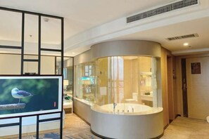A modern bathroom with a glass-enclosed bathtub, a television, and a bird on a perch. - Golden Phoenix Hotel Luohe (Luohe)