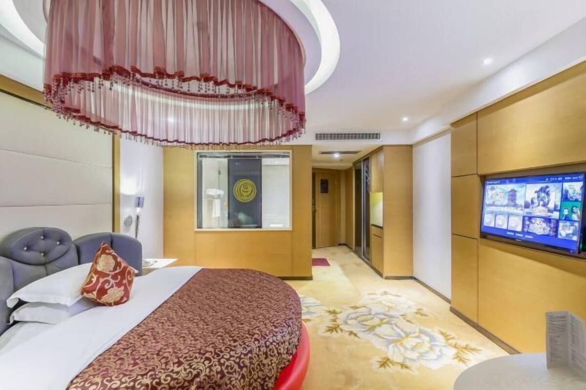 Habitación de hotel con cama, televisión, escritorio y un espejo grande.