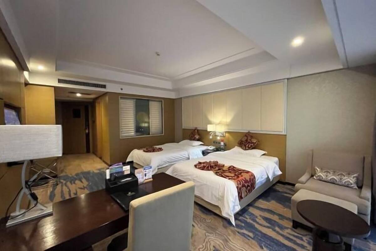 Habitación de hotel con dos camas, un escritorio, una silla, una mesita y un sofá.