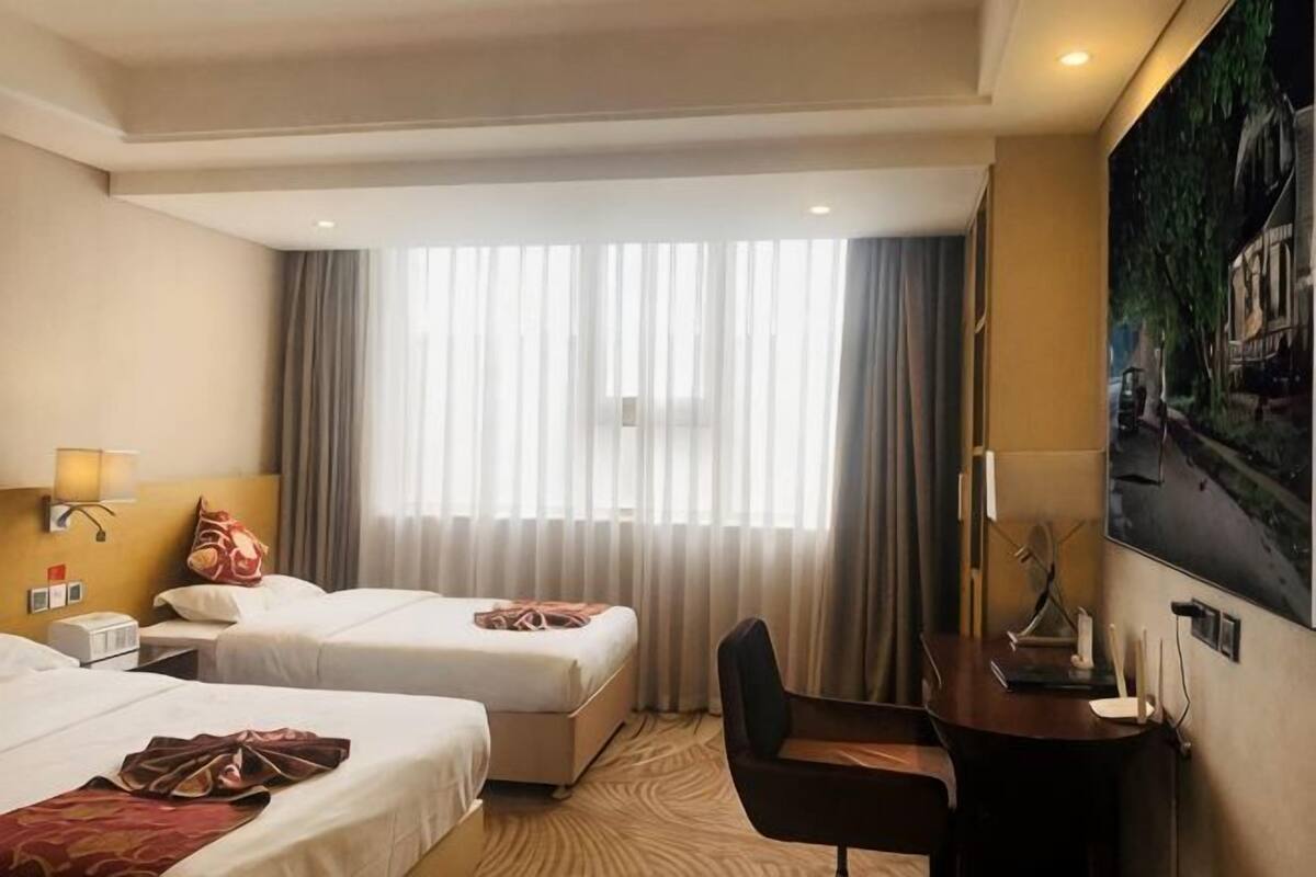 Habitación de hotel con dos camas, un escritorio, una silla, una lámpara, un cuadro y una ventana con cortinas.