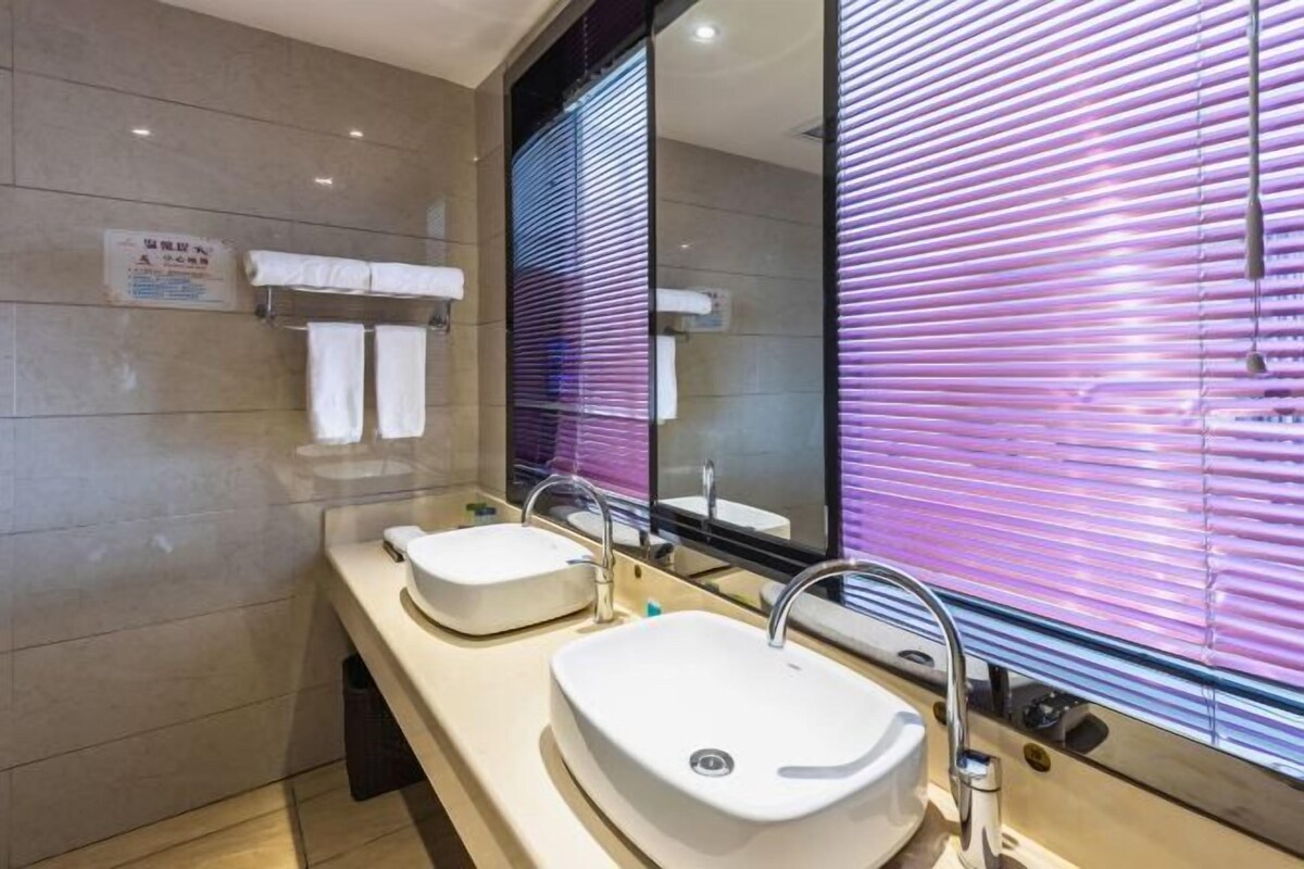 A modern bathroom with two sinks, a large mirror, and a window with purple blinds.