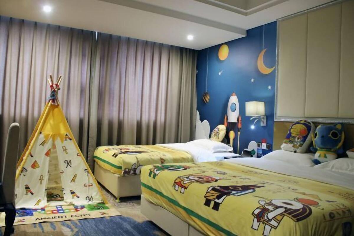 Habitación de hotel con dos camas, una tienda de campaña, un mural del cielo nocturno y decoración con luna y estrellas.