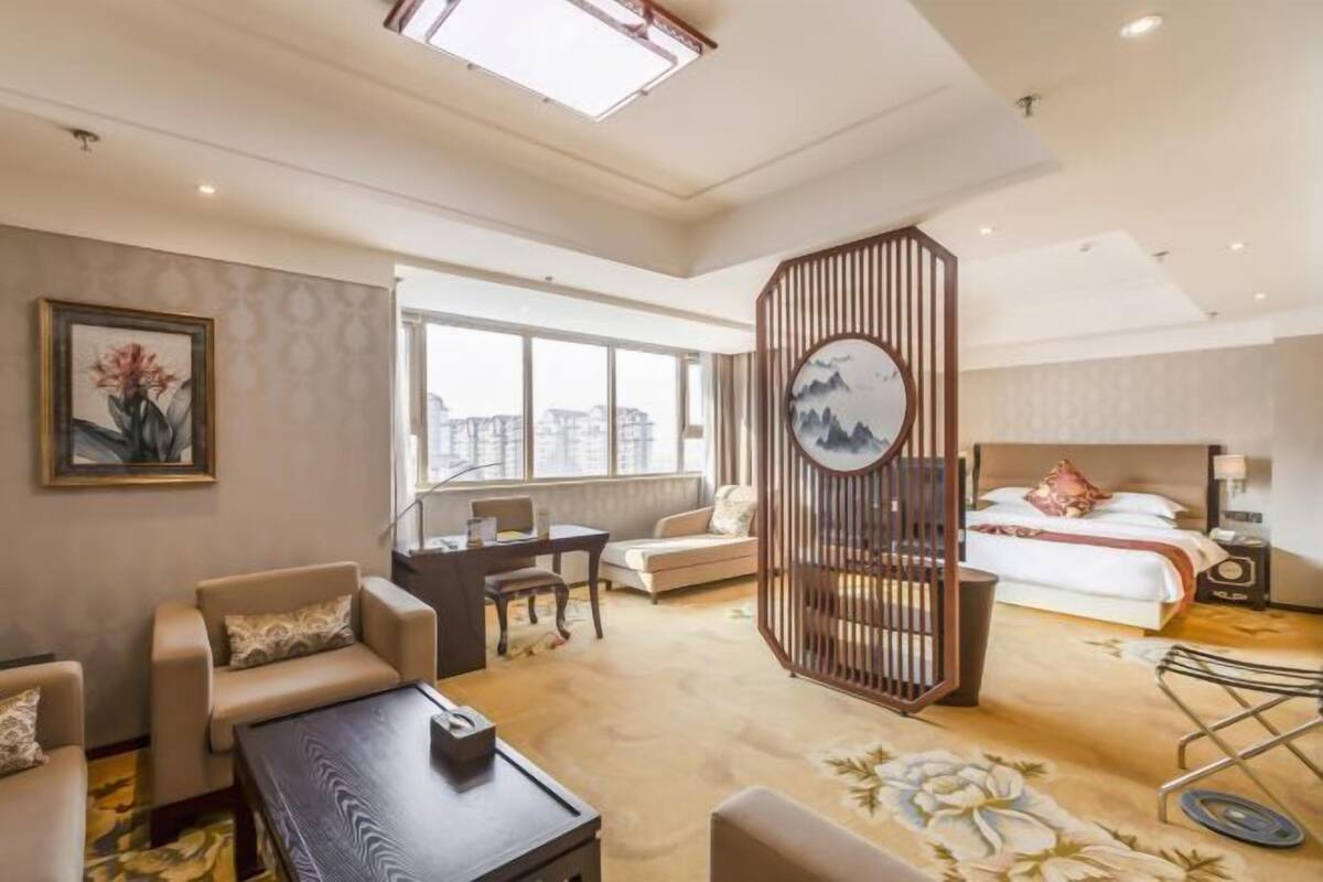 Habitación de hotel con cama, escritorio, sillón, sofá, biombo decorativo y una ventana grande.