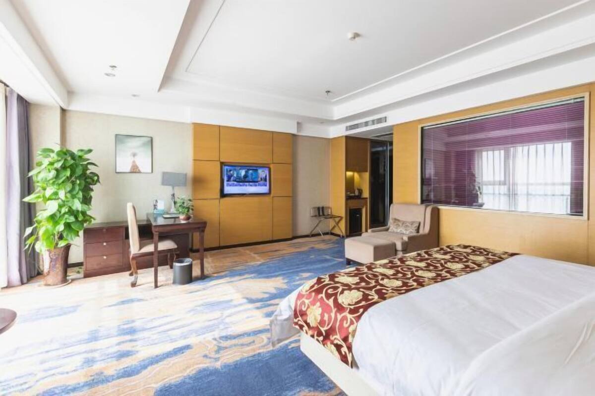 Una habitación de hotel con cama, escritorio, silla, televisor y un amplio ventanal.