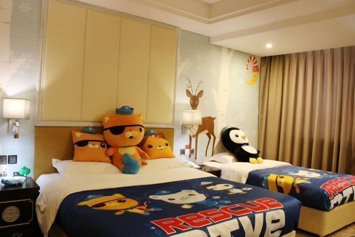 Habitación de hotel con dos camas, cada una con una colcha temática de 'Rescue Mission', una mesita de noche, una lámpara y una pared decorada con un ciervo y un pingüino.