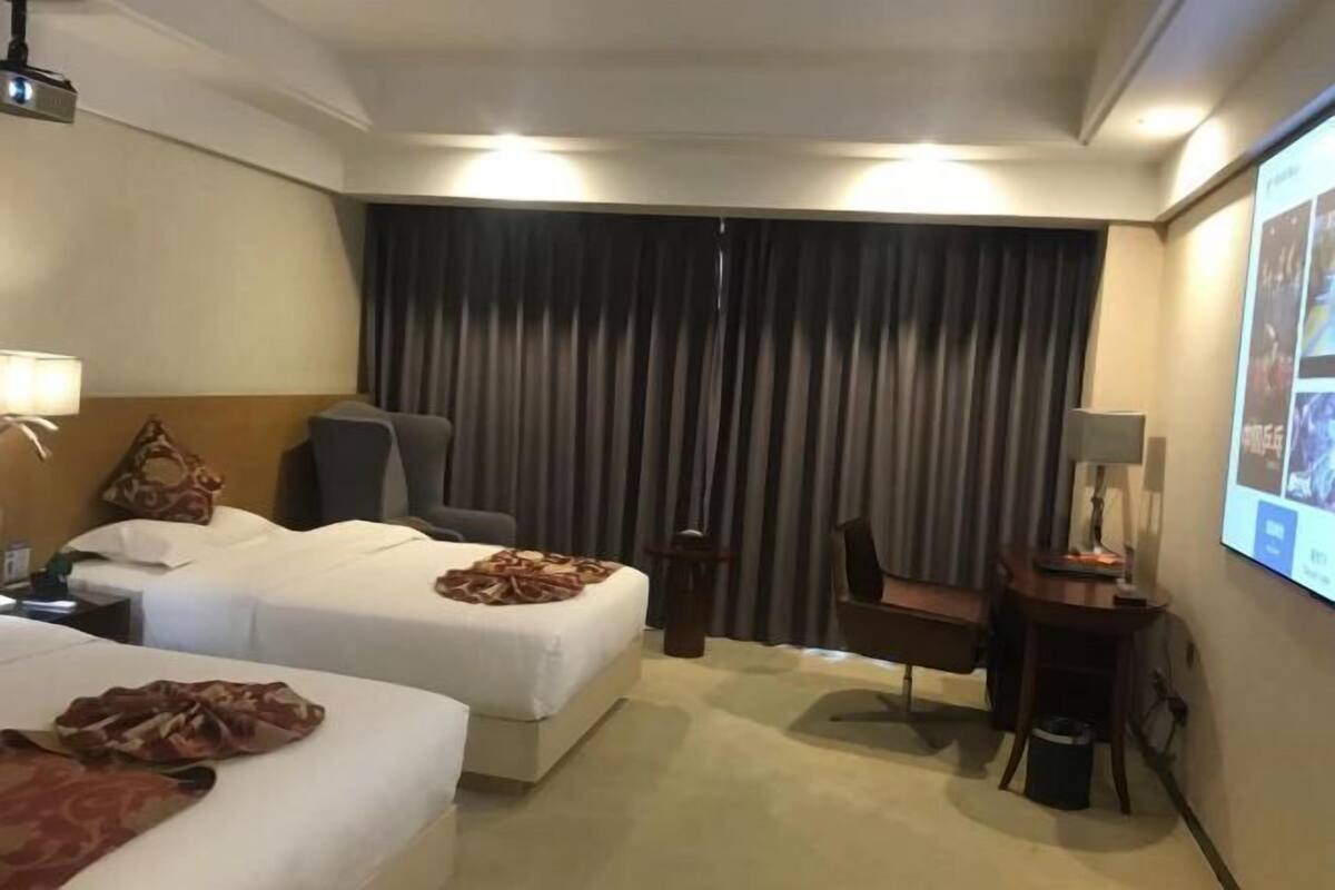 Habitación de hotel con dos camas, un escritorio, una silla, una pantalla para proyector y una cortina.