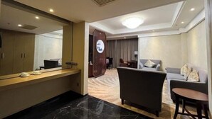 Camera d'albergo con un grande specchio, un divano, un tavolino e una zona salotto separata con una poltrona e un divano.