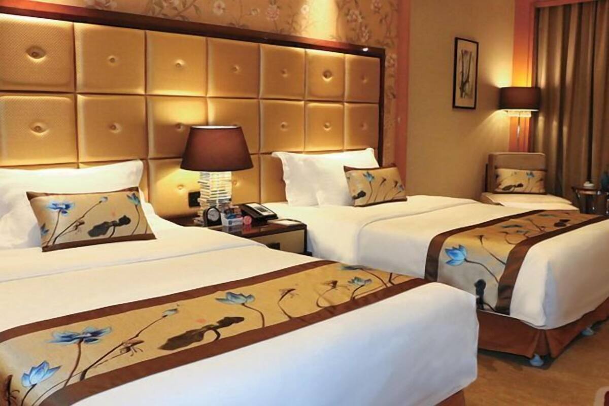A hotel room with two beds, a large padded headboard, bedside lamps, and floral-patterned bedspreads.