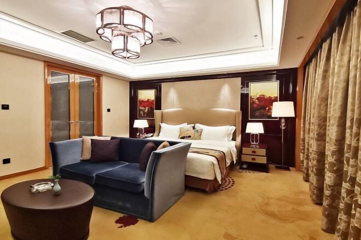 A hotel room with a bed, a sofa, a small table, and a lamp.