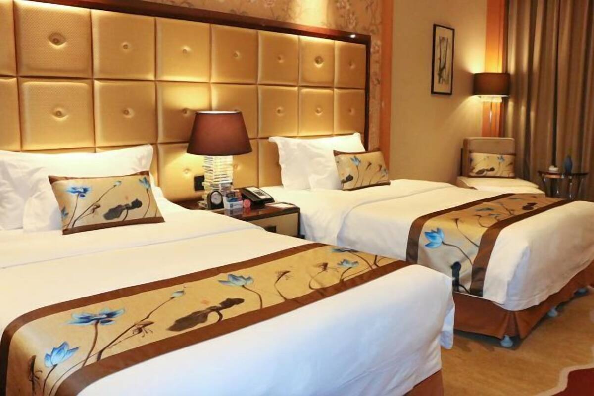 A hotel room with two beds, a headboard, bedside lamps, and a nightstand with a phone.